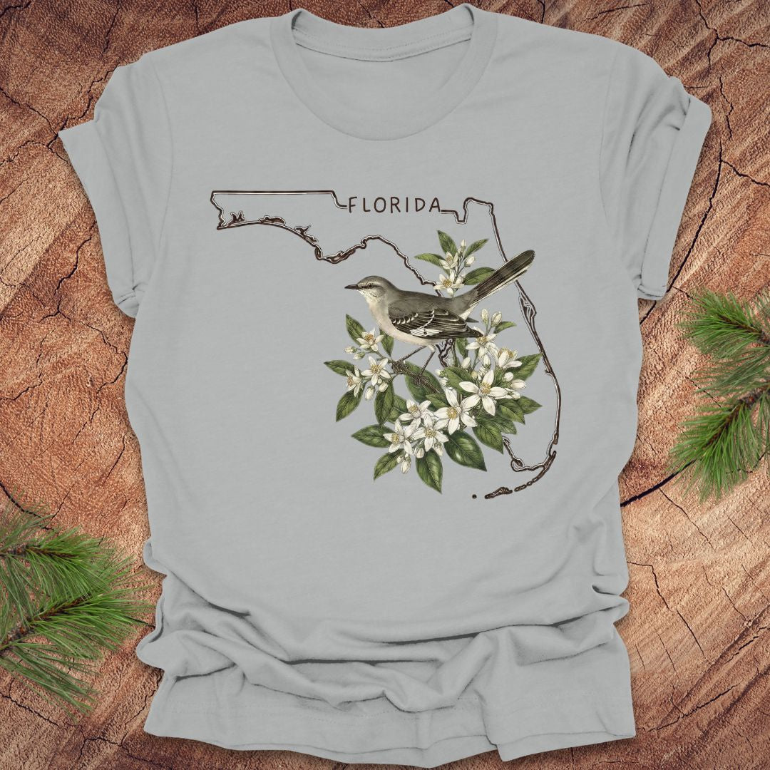 Gray t-shirt with Florida outline, mockingbird, and flowers on a wooden surface