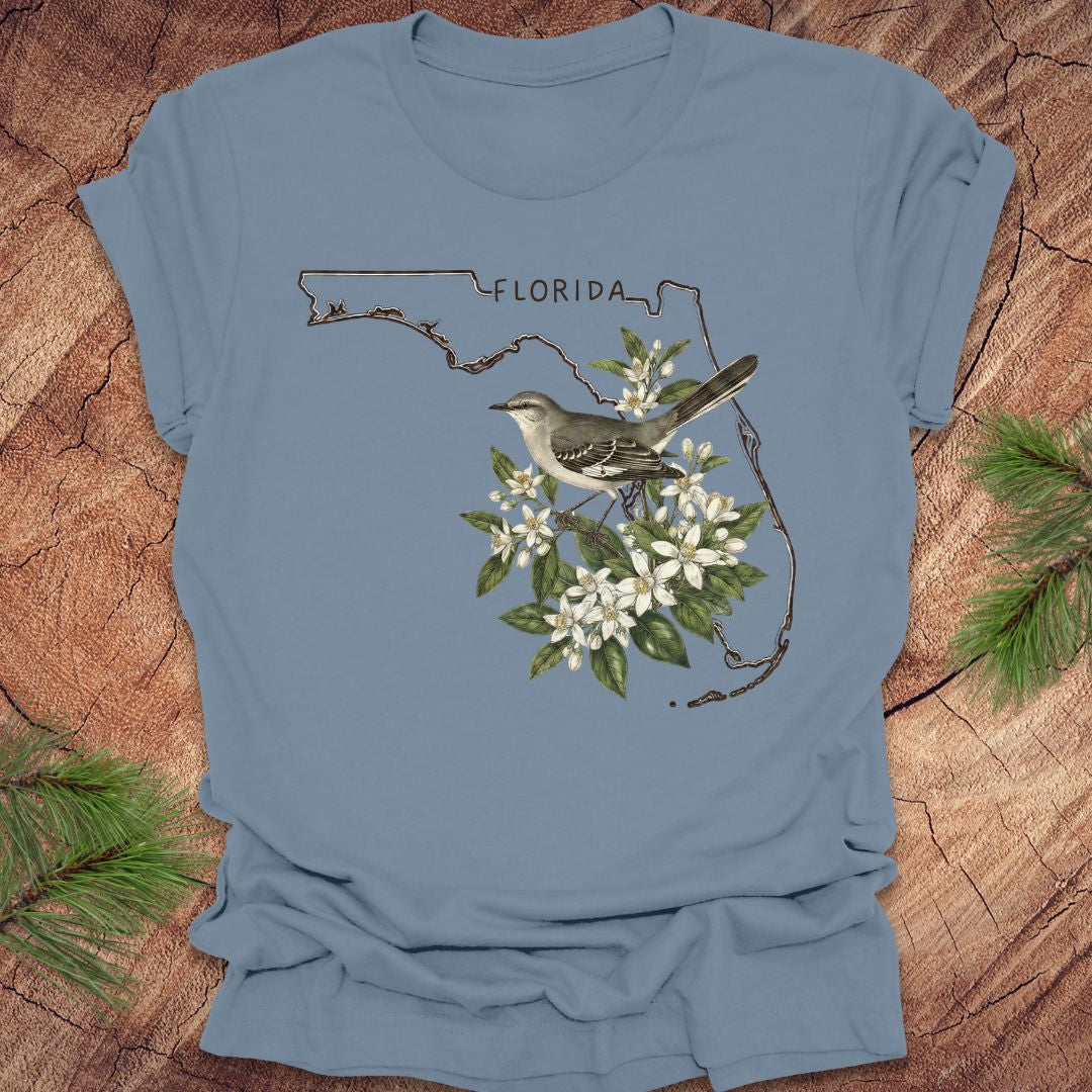 Blue t-shirt with Florida outline, mockingbird, and flowers on a wooden surface