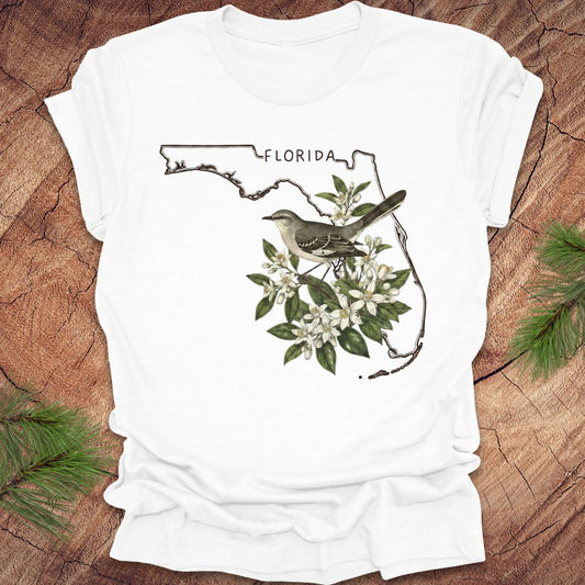 White t-shirt with Florida map and mockingbird design on a wooden surface