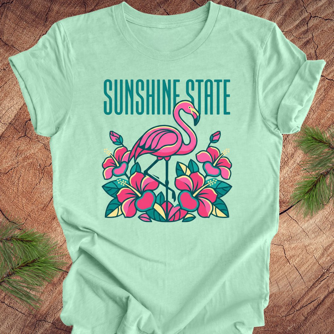 Mint green t-shirt with a pink flamingo graphic and 'Sunshine State' text on a wooden surface.