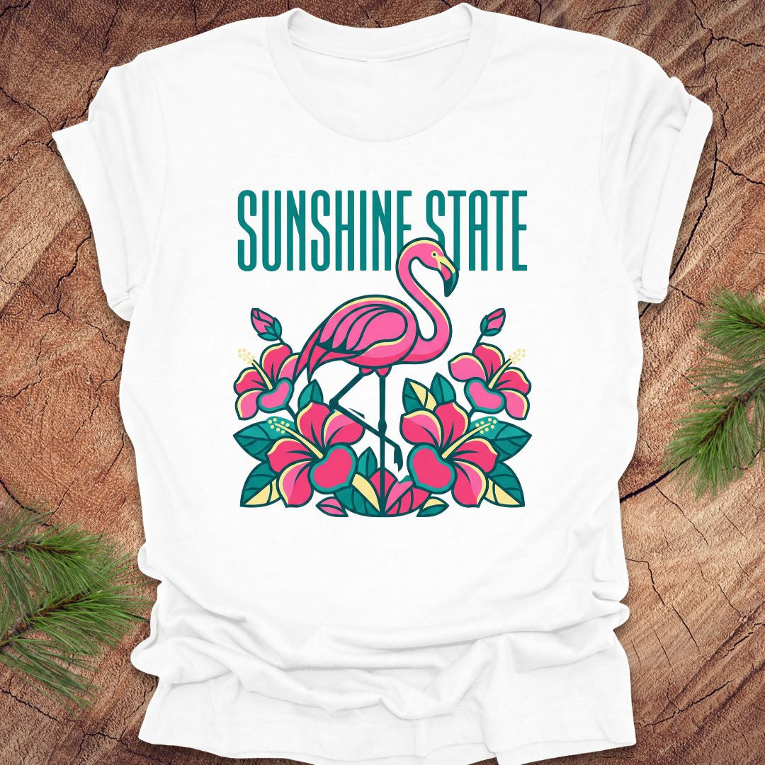 White t-shirt with a pink flamingo and floral design on a wooden surface