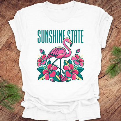 White t-shirt with a pink flamingo and floral design on a wooden surface