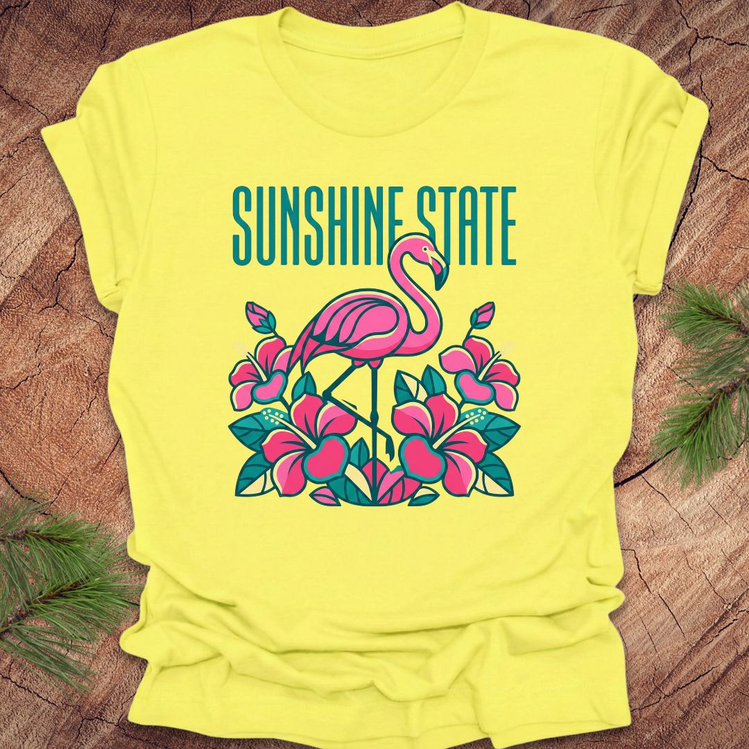 Yellow t-shirt with a flamingo graphic and 'Sunshine State' text on a wooden surface.