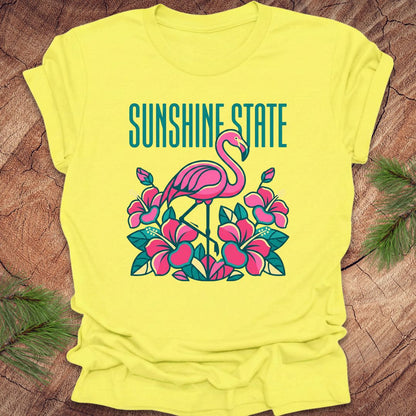 Yellow t-shirt with a flamingo graphic and 'Sunshine State' text on a wooden surface.