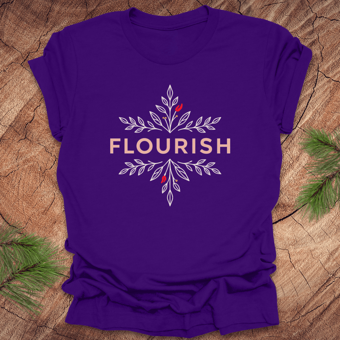 Purple t-shirt with 'FLOURISH' design and flowers on a wooden surface with greenery.