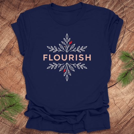 Navy blue t-shirt with 'FLOURISH' design and flowers on a wooden surface with greenery.