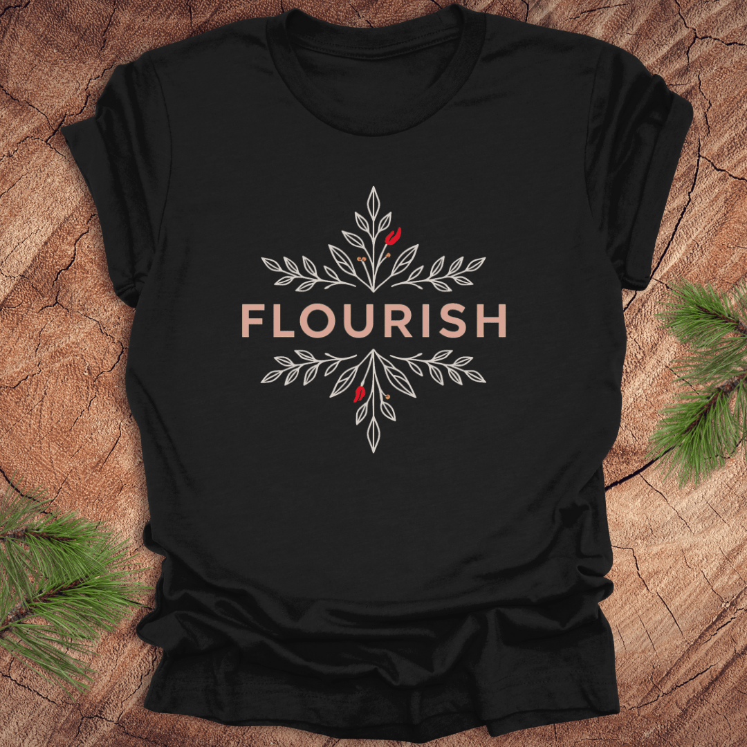 Black t-shirt with 'FLOURISH' design and flowers on a wooden surface with greenery.