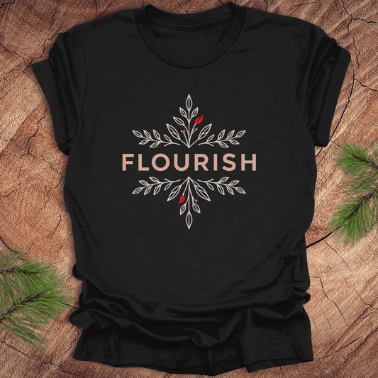 Black t-shirt with 'FLOURISH' design and flowers on a wooden surface with greenery.