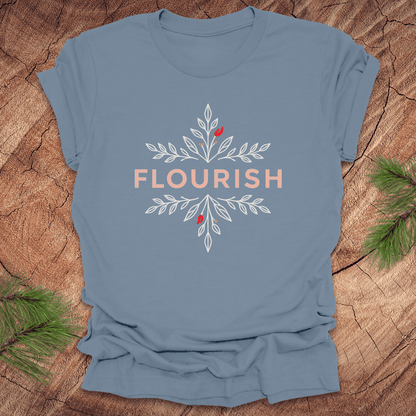 Steel blue t-shirt with 'FLOURISH' design and flowers on a wooden surface with greenery.