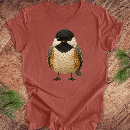 Clay colored t-shirt with a chickadee made of flowers on a wood background.