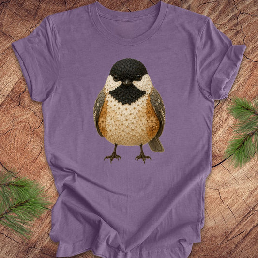Purple t-shirt with a chickadee made of flowers on a wood background.