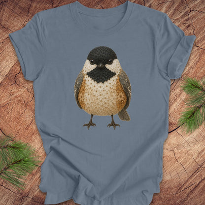 Blue t-shirt with a chickadee made of flowers on a wood background.