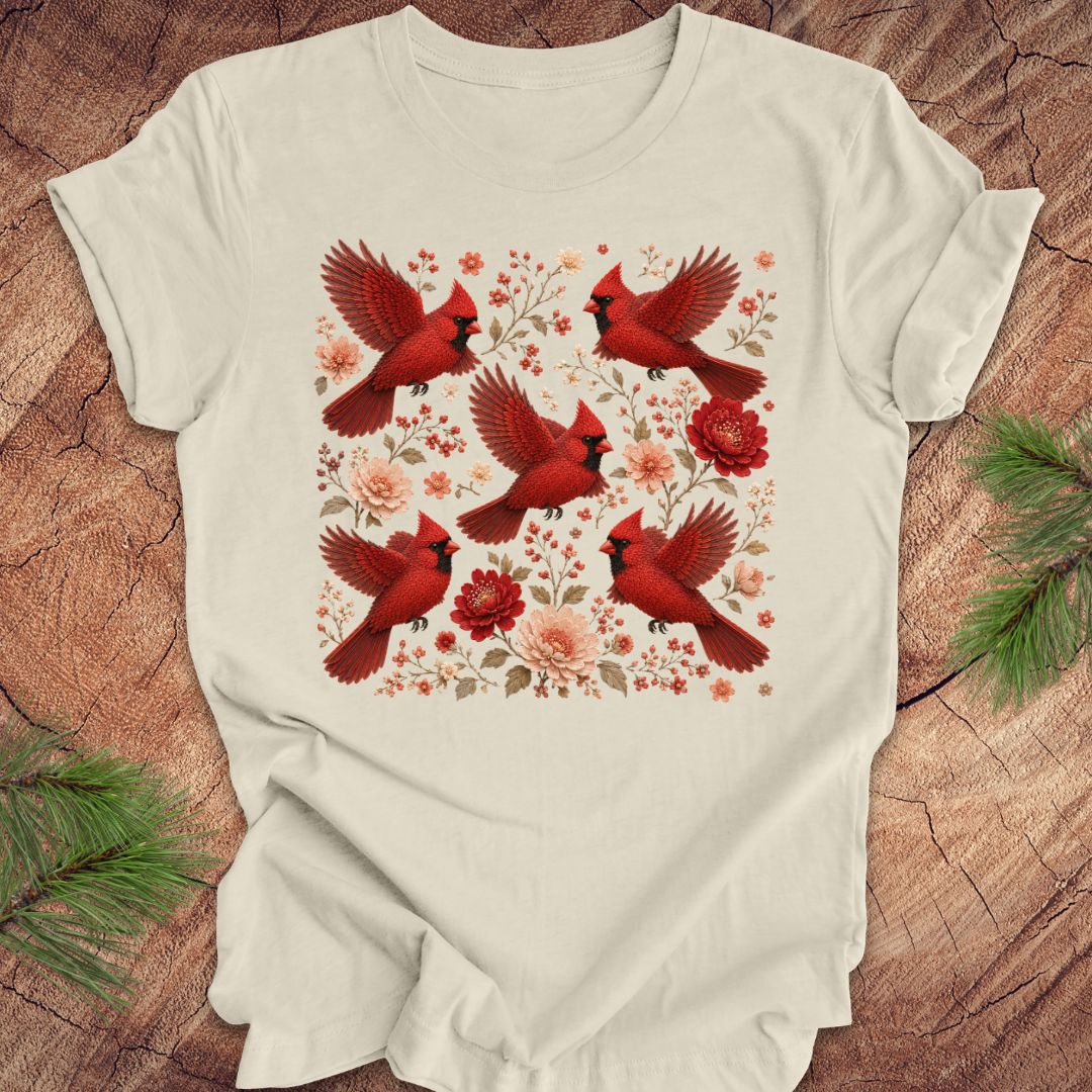 Beige t-shirt with cardinals and flowers on a wood background.