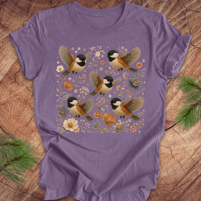 Purple t-shirt with chickadees and flowers on a wood background.