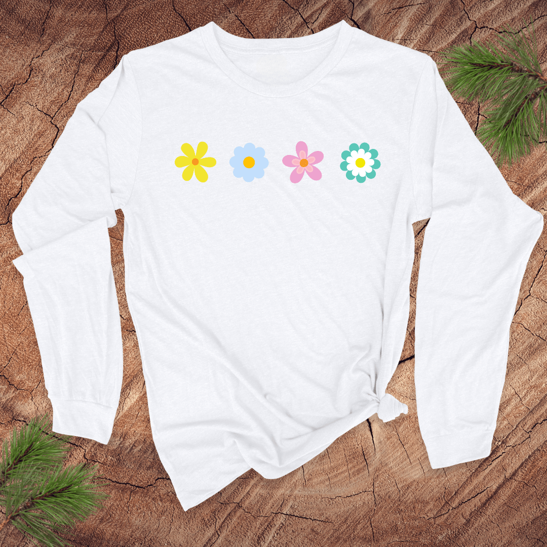 A white long-sleeve shirt with colorful flower designs on a wooden surface with pine branches