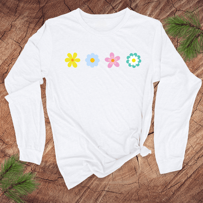 A white long-sleeve shirt with colorful flower designs on a wooden surface with pine branches