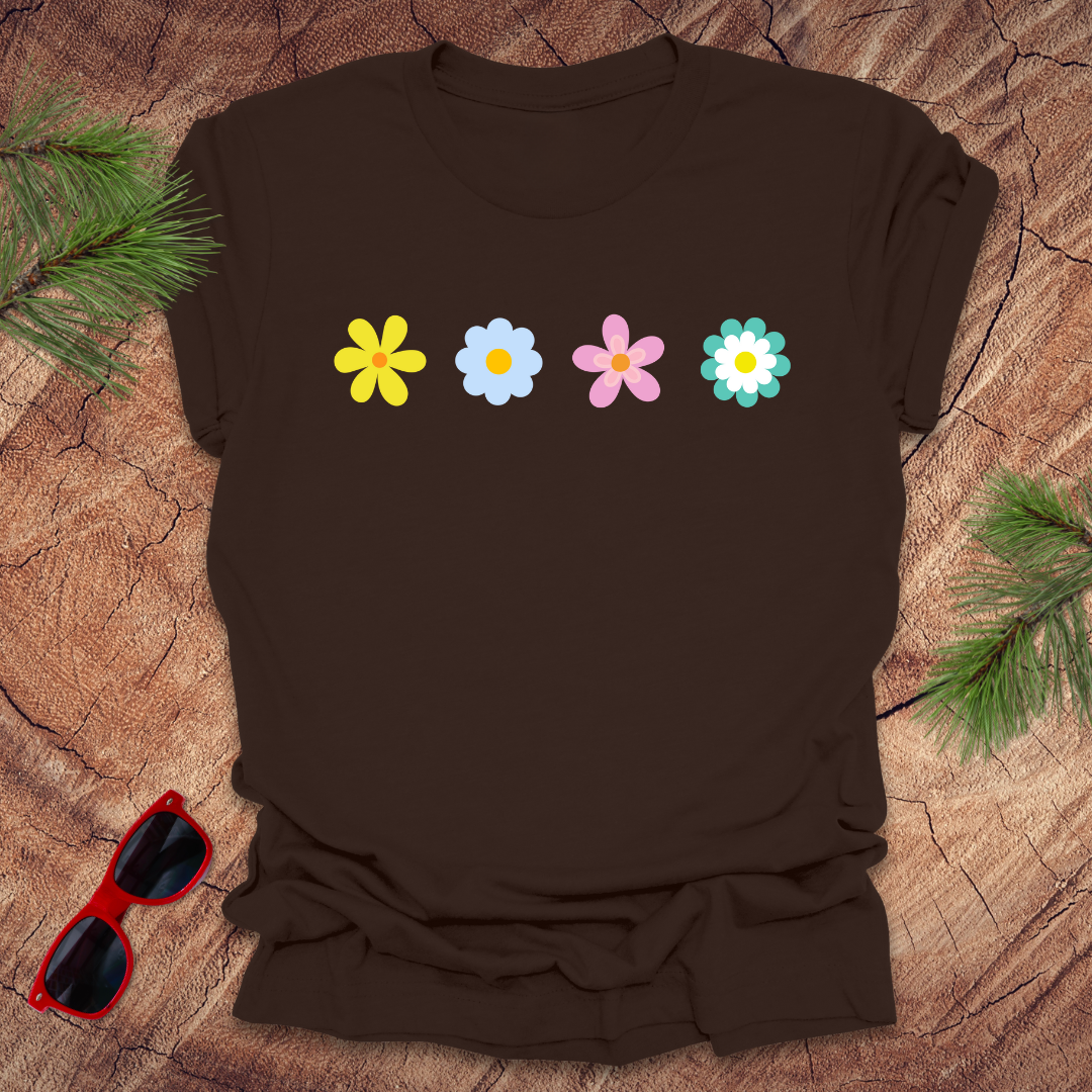 Brown t-shirt with colorful flower designs on a wooden surface with sunglasses and greenery.