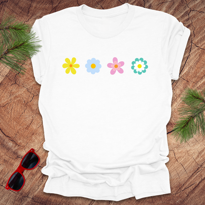 White t-shirt with colorful flower designs on a wooden surface with sunglasses and greenery.