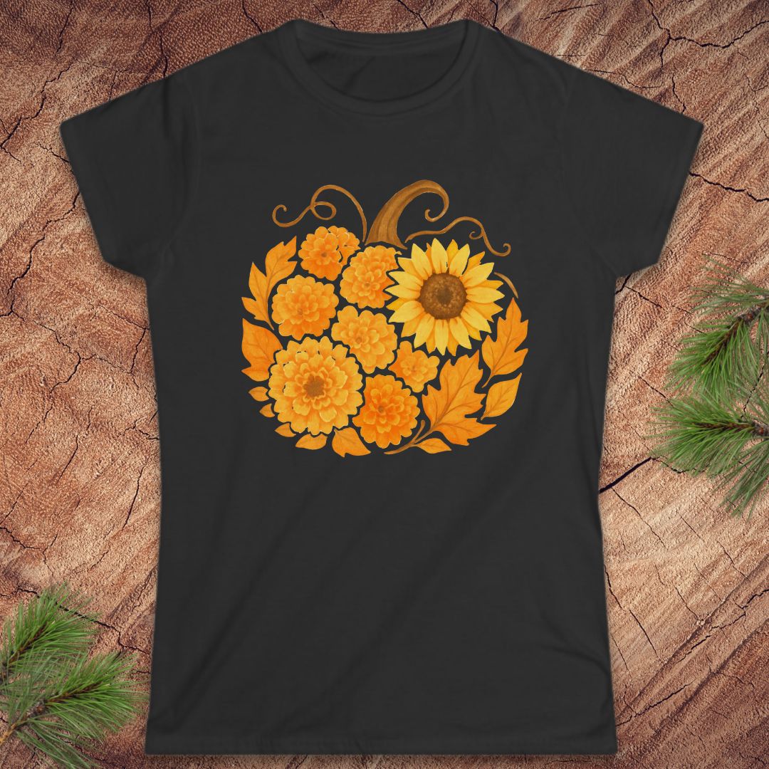 A black short-sleeve crewneck t-shirt featuring a graphic of a pumpkin made from yellow and orange flowers, displayed flat on a rustic wood background with pine needles.