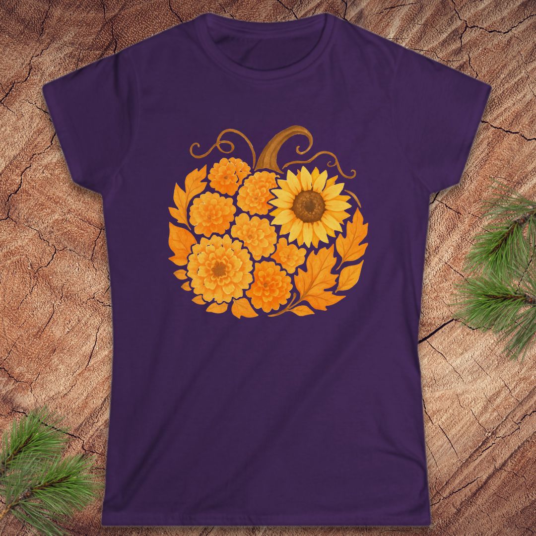 A purple short-sleeve crewneck t-shirt featuring a graphic of a sunflower and marigolds arranged in a pumpkin shape, displayed flat on a textured wood background with pine branches in the corners.