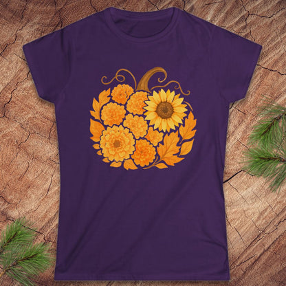 A purple short-sleeve crewneck t-shirt featuring a graphic of a sunflower and marigolds arranged in a pumpkin shape, displayed flat on a textured wood background with pine branches in the corners.