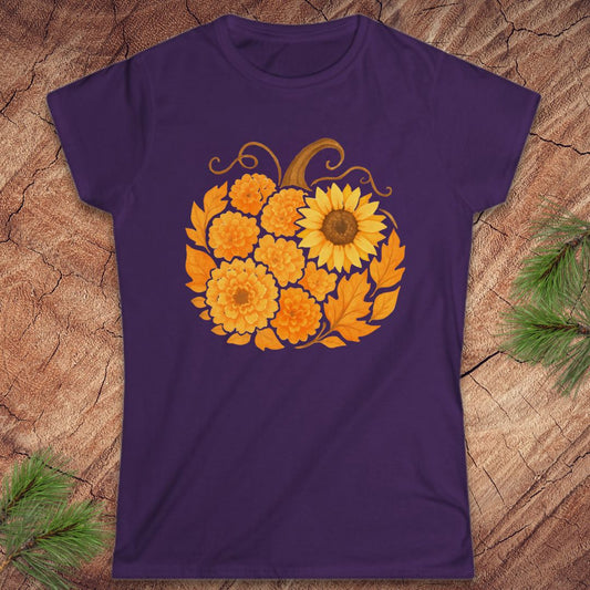 A purple short-sleeve crewneck t-shirt featuring a graphic of a sunflower and marigolds arranged in a pumpkin shape, displayed flat on a textured wood background with pine branches in the corners.