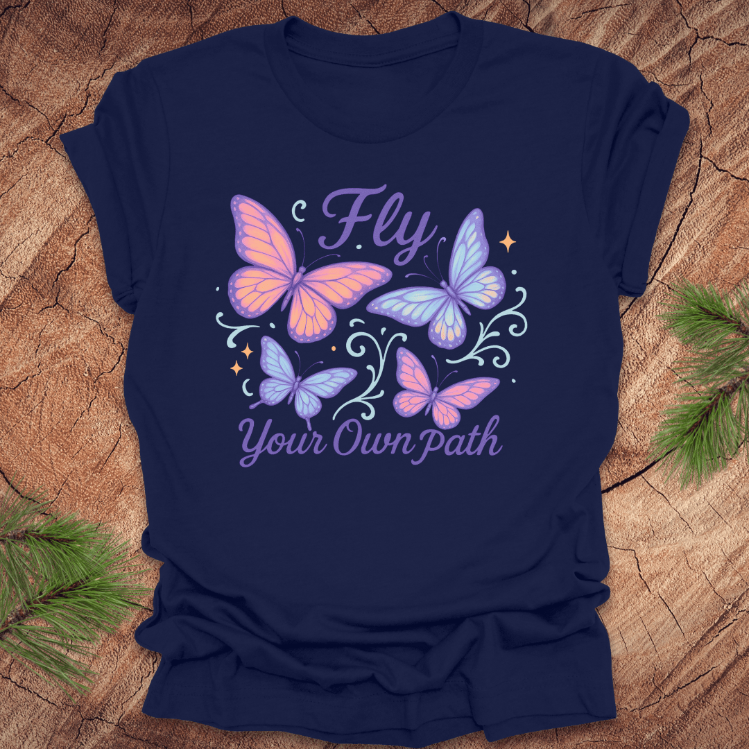 Navy blue t-shirt with butterfly design and 'Fly Your Own Path' text on a wooden surface.