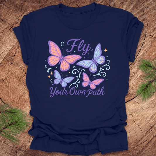 Navy blue t-shirt with butterfly design and 'Fly Your Own Path' text on a wooden surface.