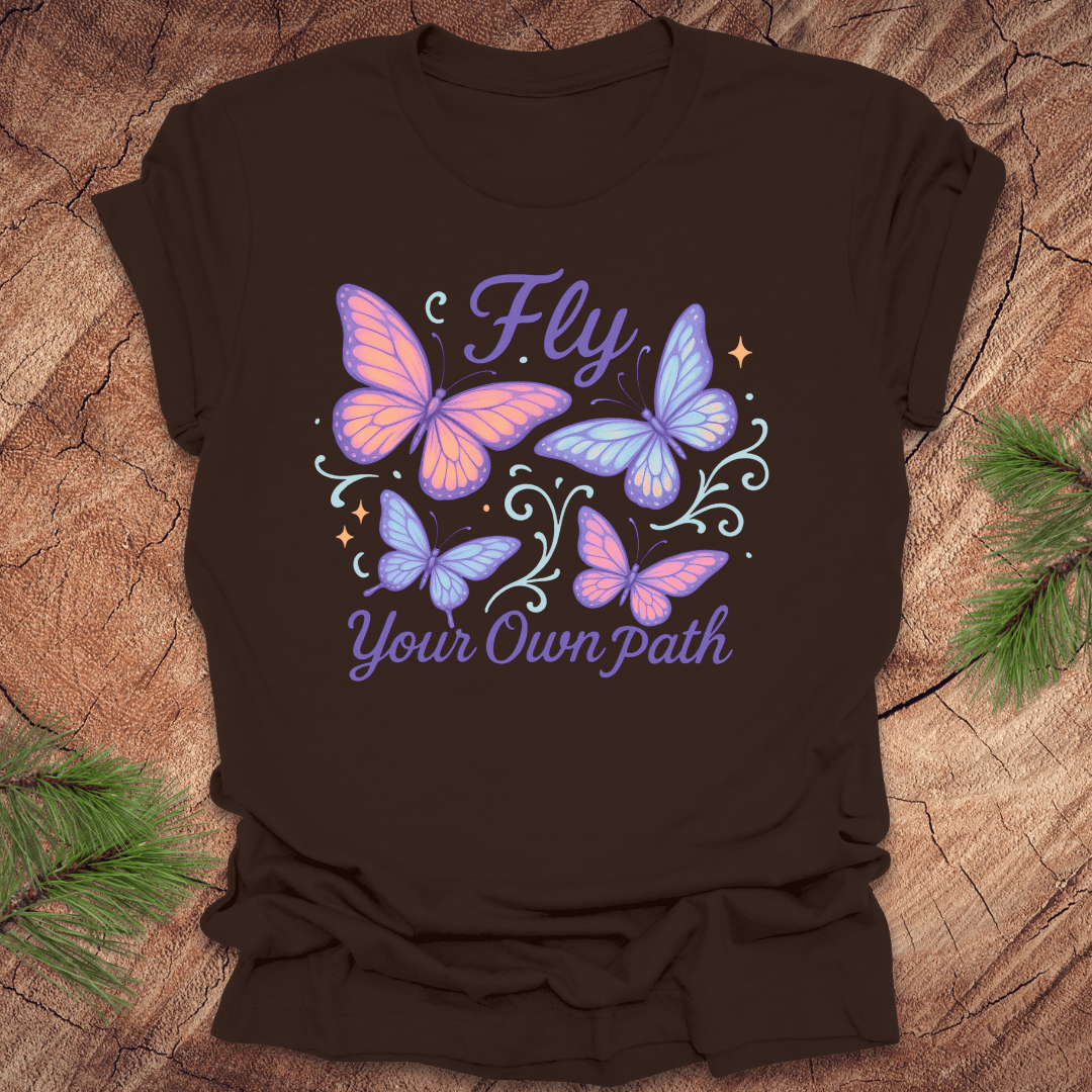 Brown t-shirt with butterfly design and 'Fly Your Own Path' text on a wooden surface.