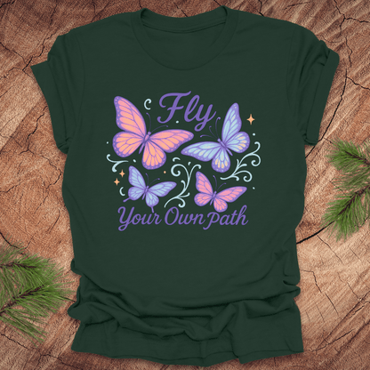 Green t-shirt with butterfly design and 'Fly Your Own Path' text on a wooden surface.
