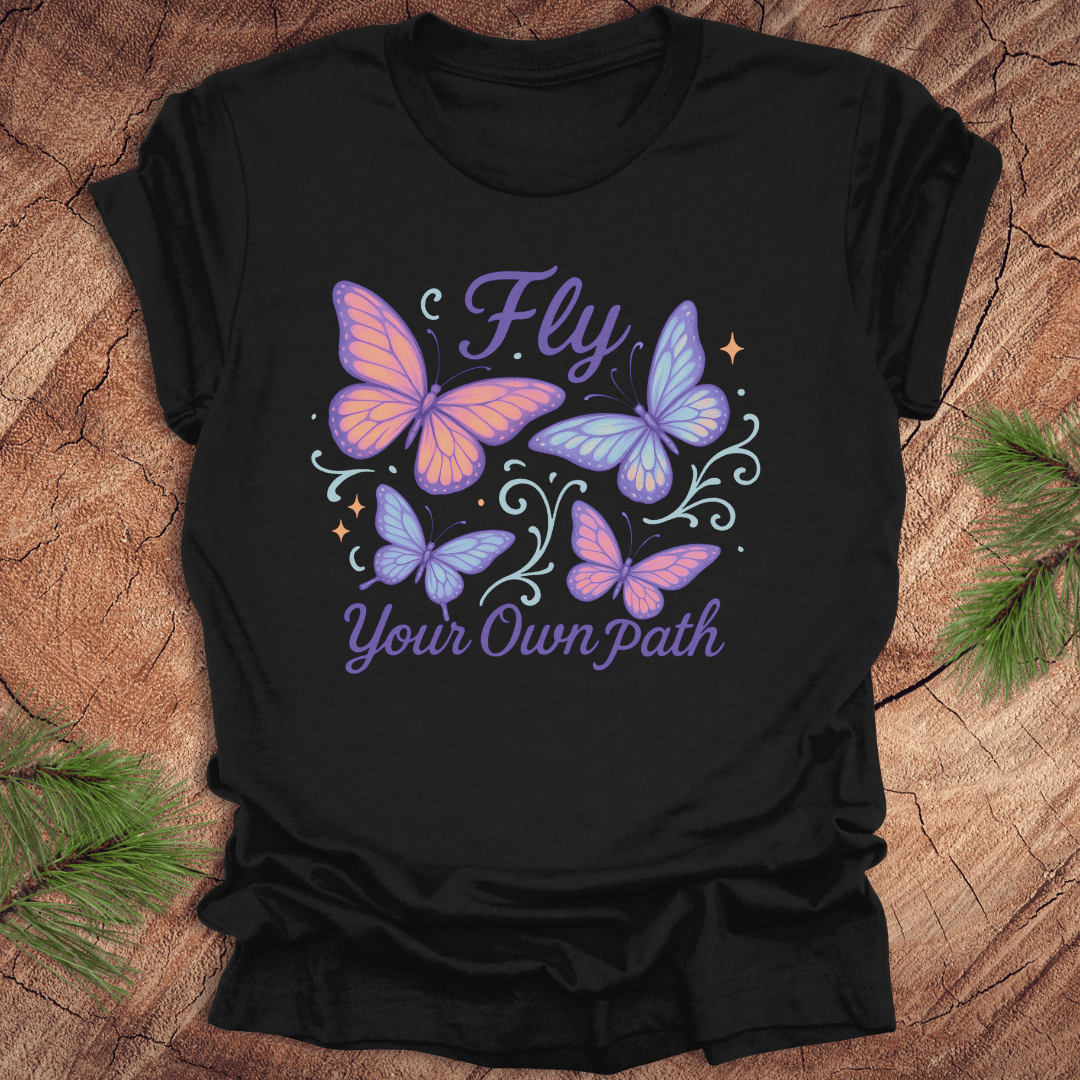Black t-shirt with butterfly design and 'Fly Your Own Path' text on a wooden surface.