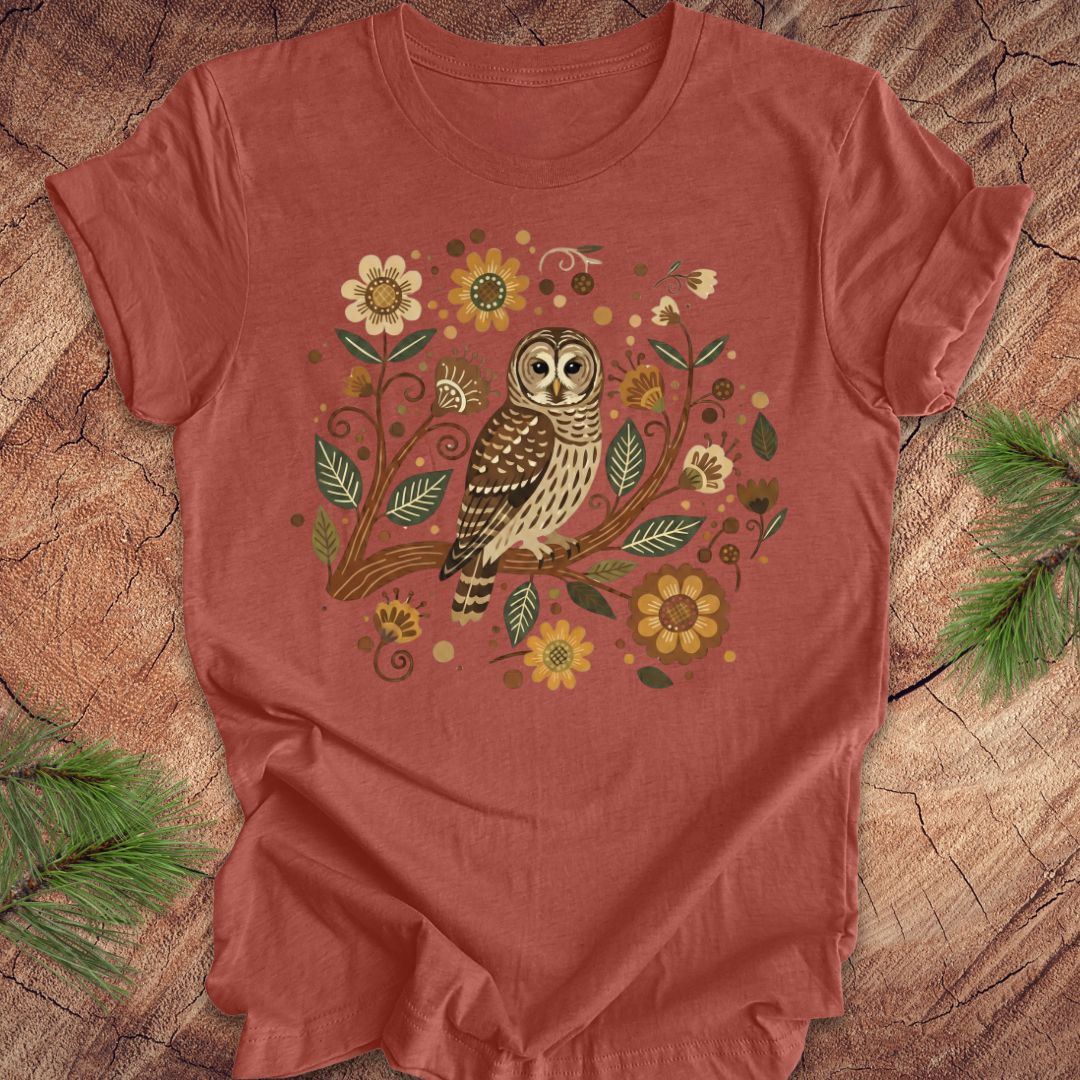 Clay colored t-shirt with an owl and floral design on a wooden surface