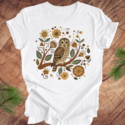 White t-shirt with an owl and floral design on a wooden surface