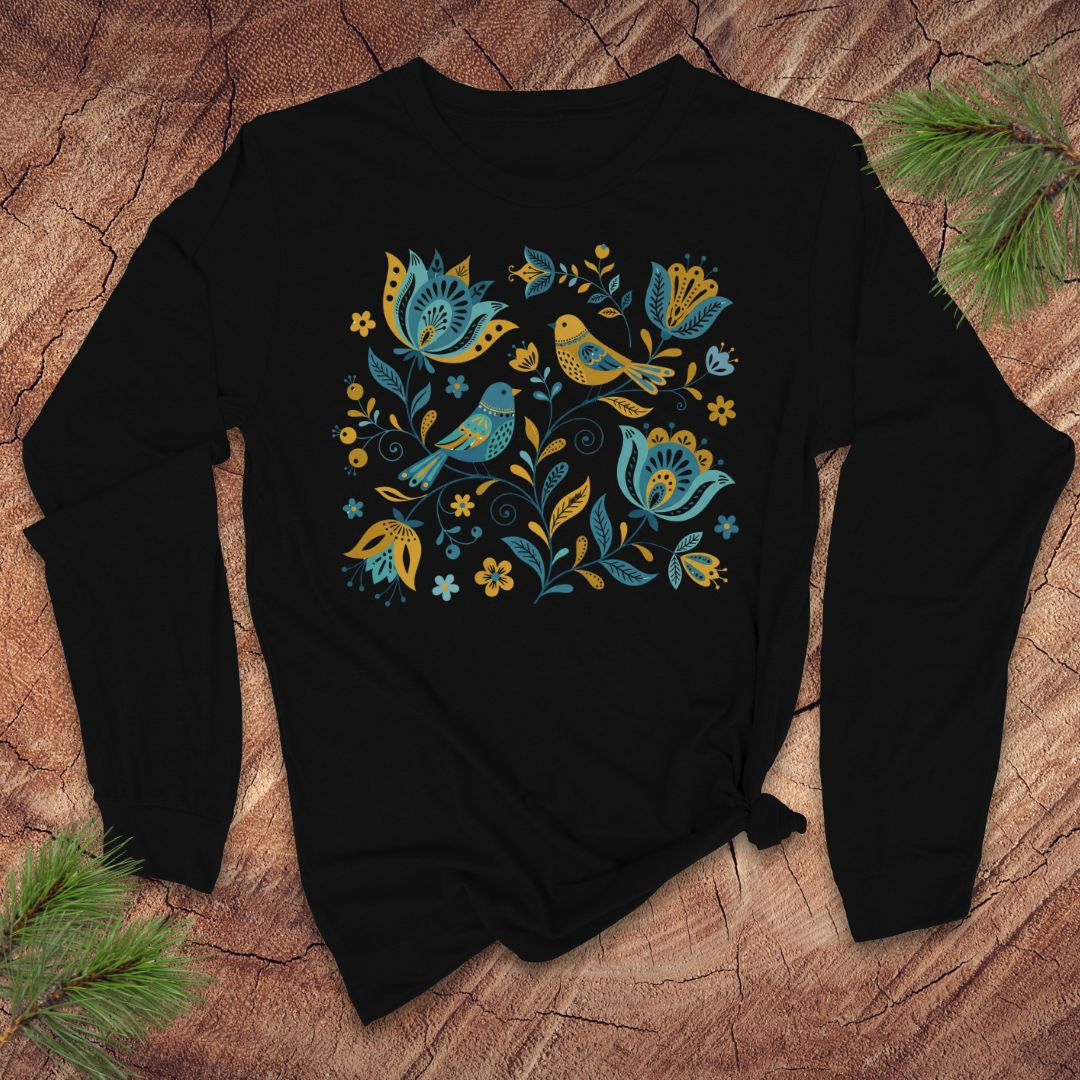 Black long-sleeve tshirt with folk art floral and bird design on a wooden surface