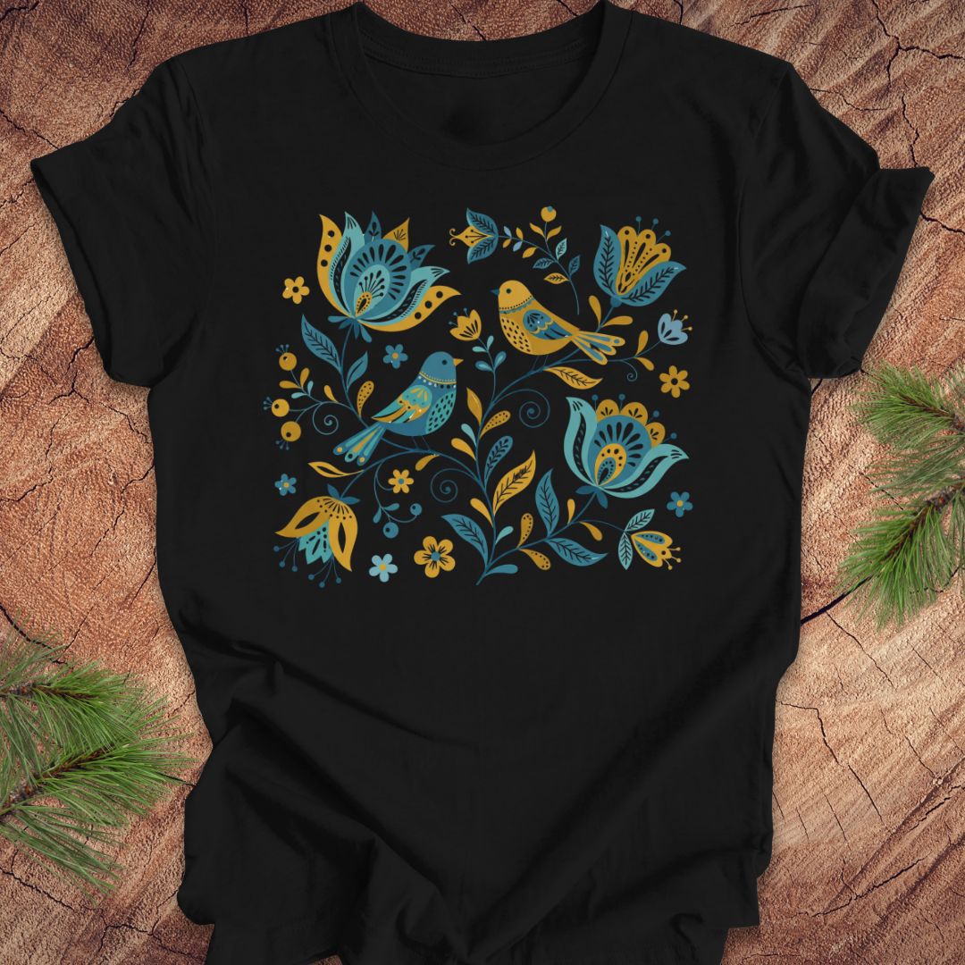 Black t-shirt with blue and yellow floral and bird design on a wooden surface.
