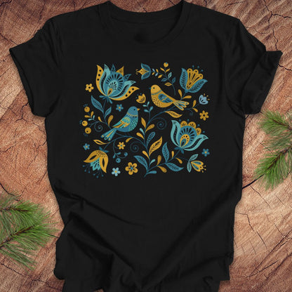 Black t-shirt with blue and yellow floral and bird design on a wooden surface.