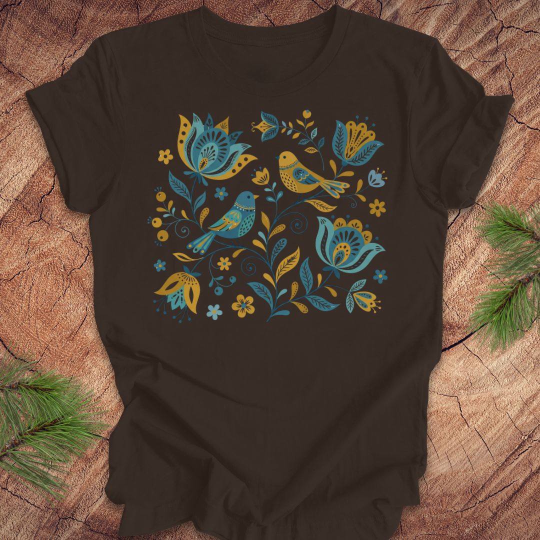 Brown t-shirt with blue and yellow floral and bird design on a wooden surface.