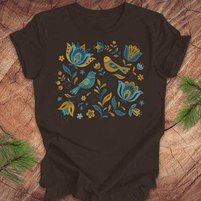 Brown t-shirt with blue and yellow floral and bird design on a wooden surface.