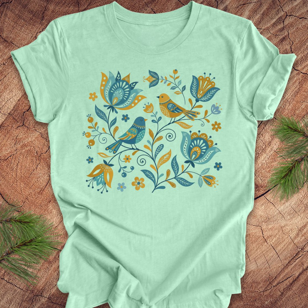 Mint green t-shirt with floral and bird design on a wooden surface