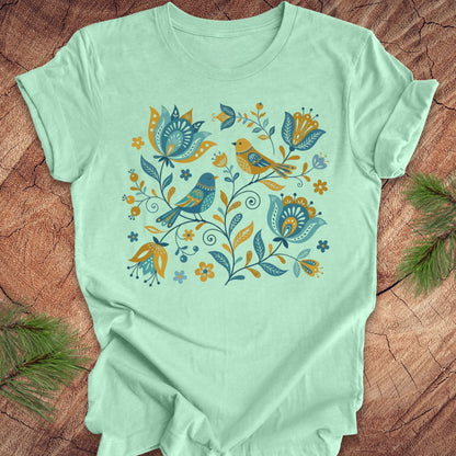 Mint green t-shirt with floral and bird design on a wooden surface
