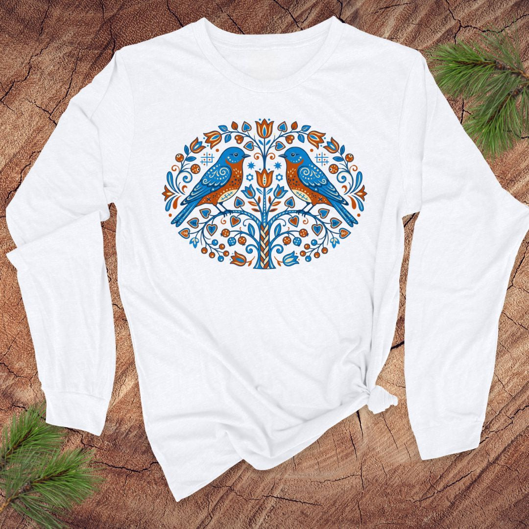 White long-sleeve shirt with a colorful tree design featuring two birds on a wooden surface.