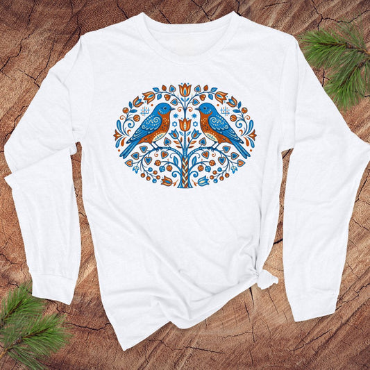 White long-sleeve shirt with a colorful tree design featuring two birds on a wooden surface.