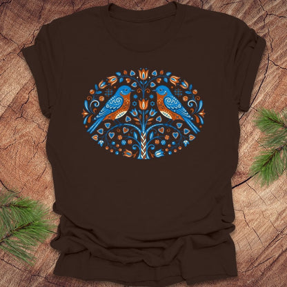 Brown t-shirt with a decorative design featuring two blue birds on a wooden surface.