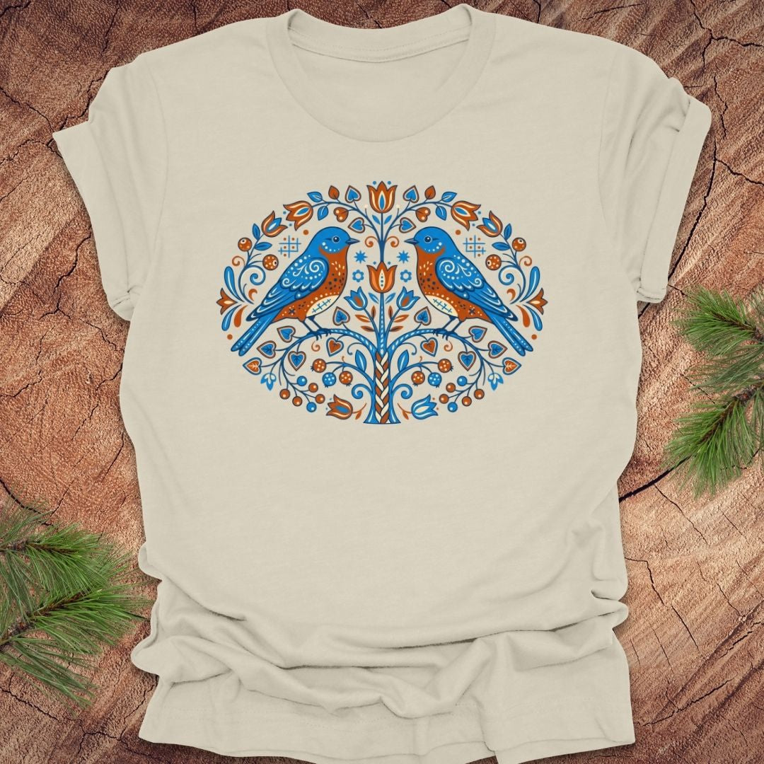Beige t-shirt with a decorative design of two birds on a wooden surface.