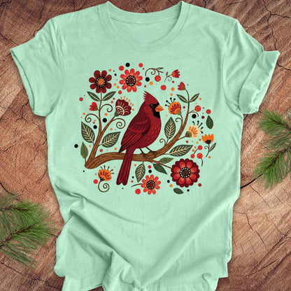 Mint green t-shirt with a red cardinal and floral design on a wooden surface.