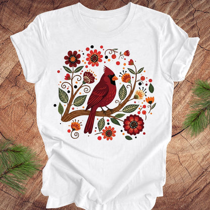 White t-shirt with a red cardinal and floral design on a wooden surface.