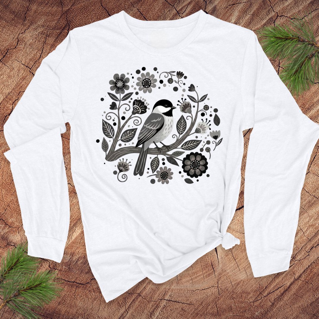 White long-sleeve shirt with a black and gray bird and floral design on a wooden surface.