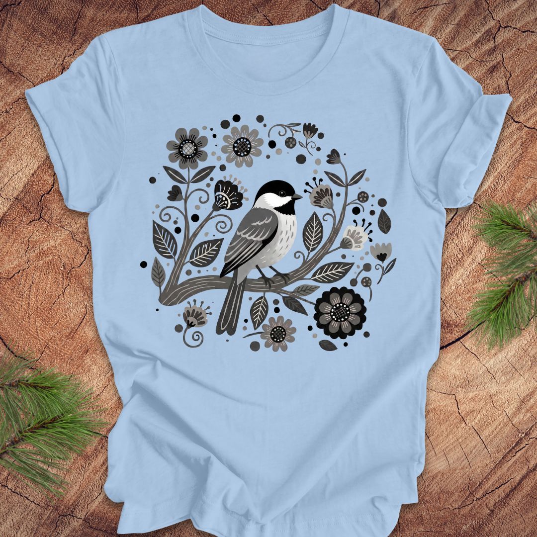 Blue t-shirt with a chickadee bird and floral design on a wooden surface