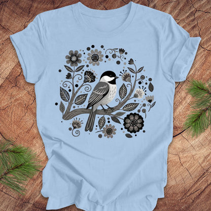 Blue t-shirt with a chickadee bird and floral design on a wooden surface