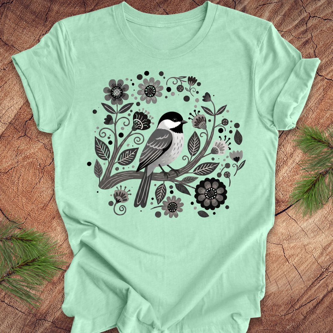 Mint green t-shirt with a bird and floral design on a wooden surface